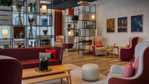 Een moderne woonkamer met een rode bank, grijze fauteuils, een houten salontafel en een boekenkast met decoratieve objecten.