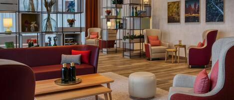 A modern living room with a red sofa, grey armchairs, a wooden coffee table, and a bookshelf with decorative items.