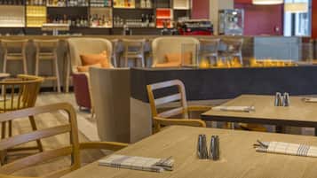 A modern restaurant with wooden tables and chairs, a bar area with shelves of bottles, and a fireplace.