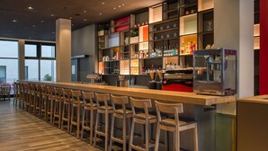 Een moderne bar met een lange toonbank, verschillende krukken en een divers aanbod aan flessen en glazen op planken.