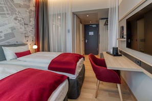 Habitación de hotel con dos camas, un escritorio, una silla, un mapa en la pared y una puerta que da a otra habitación.