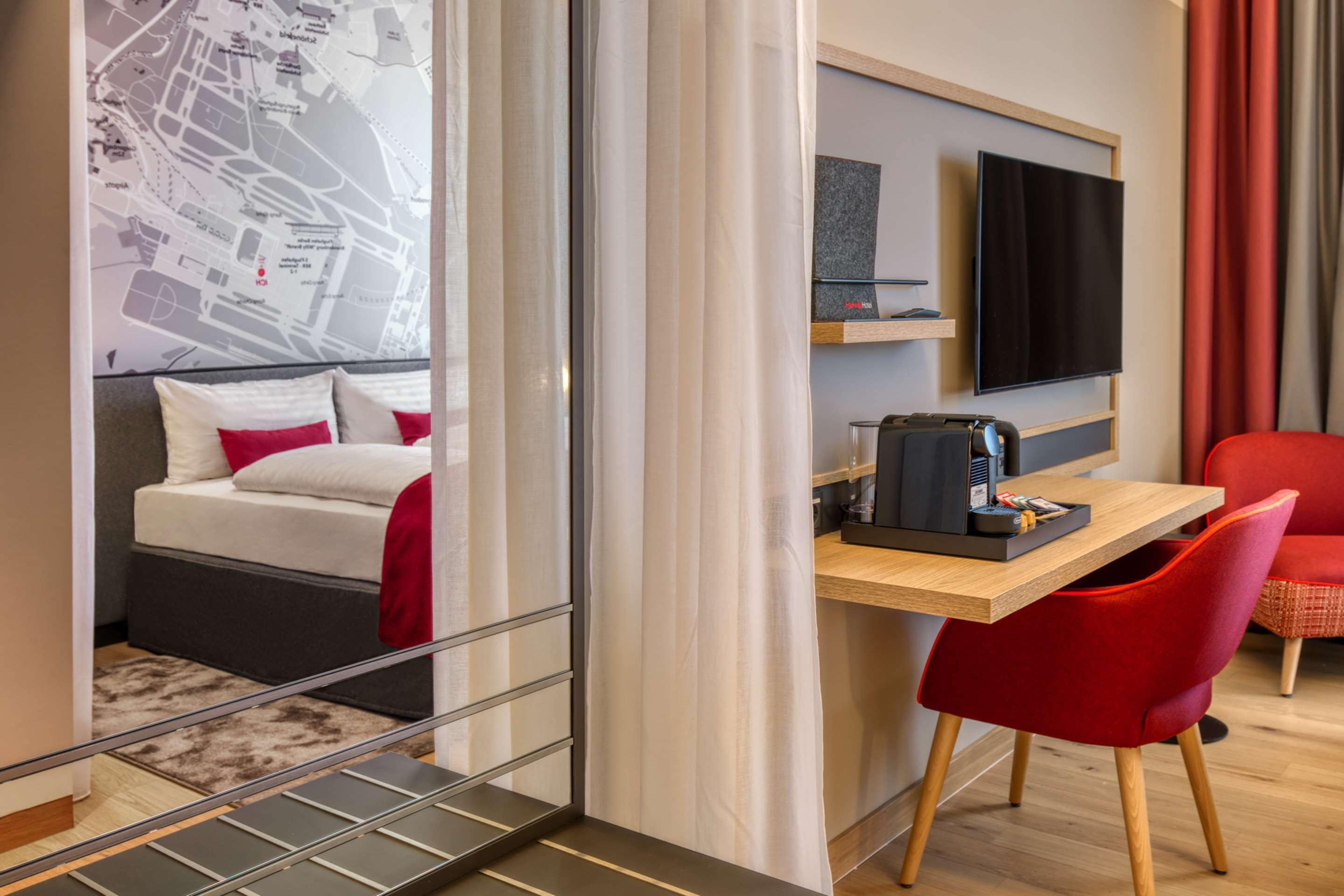 A hotel room with a bed, a desk with a computer, a TV, and a red chair.