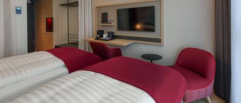 A hotel room with two beds, a TV, a small table with a coffee maker, and a red chair.