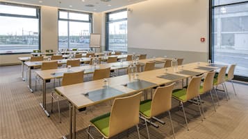 Un salón de conferencias con varias mesas y sillas, ventanas amplias y una pizarra.