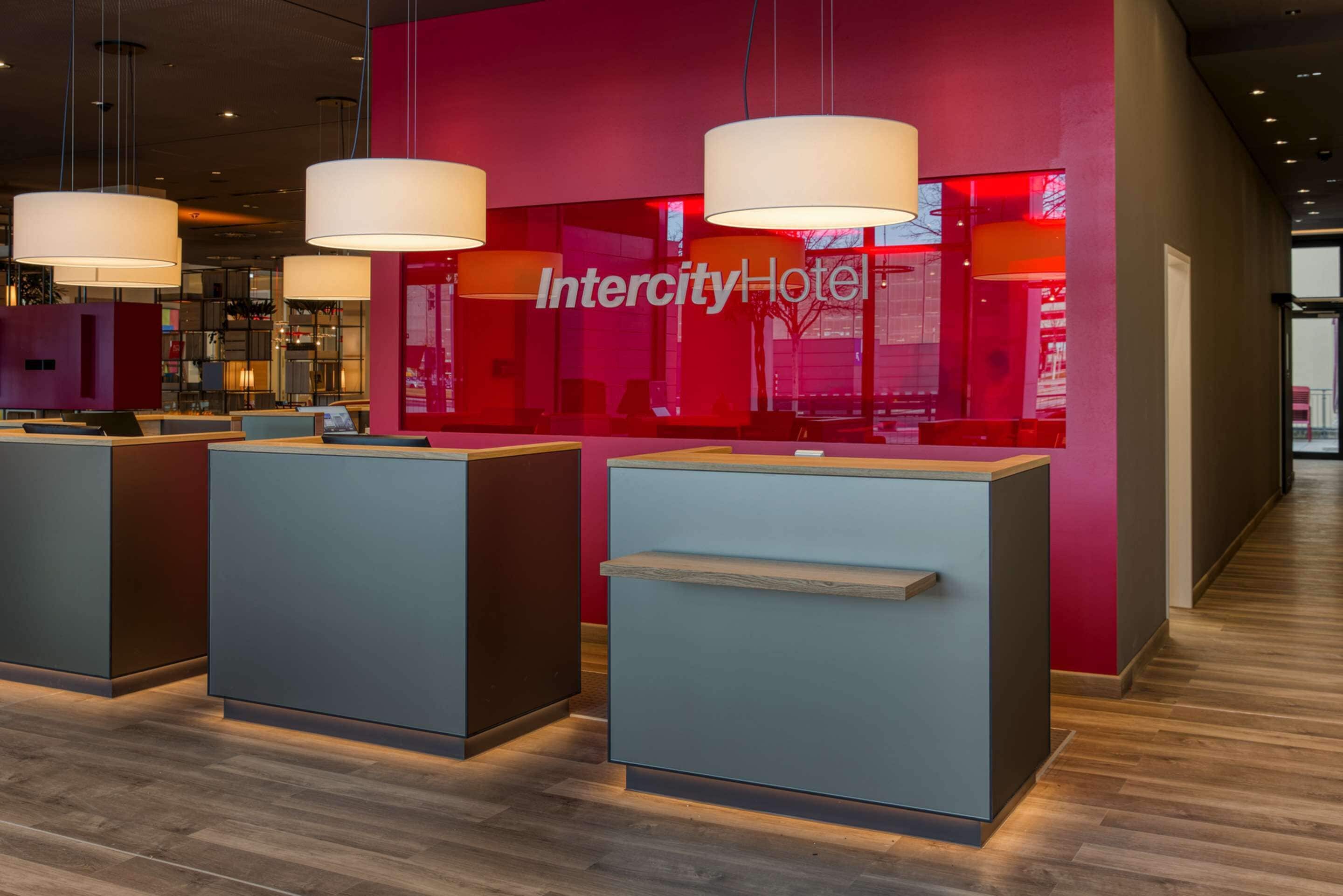 Una zona de recepción con diseño moderno, con una paleta de colores rojo y gris, y tres grandes lámparas colgantes.