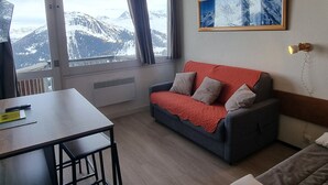 Ein Zimmer mit einem roten Sofa, einem Tisch und einem großen Fenster mit Blick auf die Berge.