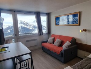 A room with a red sofa, a table, and a large window offering a mountain view.