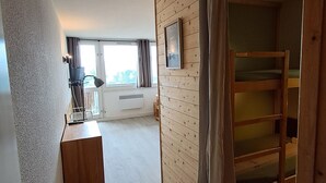 Ein Zimmer mit einem Etagenbett, einem Schreibtisch mit Lampe, einem Fenster mit Vorhängen und einem gerahmten Bild an der Wand.