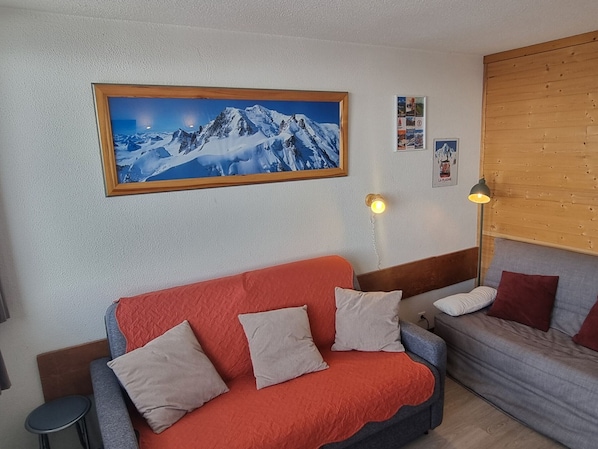 A cozy room with a red sofa, a grey sofa, and a wooden headboard.