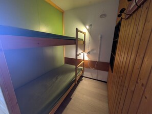 A bunk bed room with a wooden floor, a green wall, and a small window.