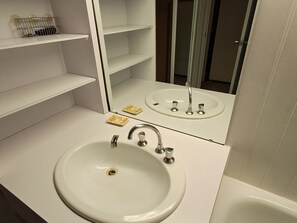 A bathroom with a white sink, a mirror, and a shelf with toiletries.