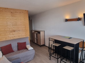 A compact living space with a sofa, a small kitchen area, and a bar stool arrangement.
