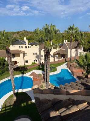 A resort with a swimming pool, palm trees, and a view of a hillside. - Lovely large penthouse apartment by golf and beach. (Dehesa de Campoamor)