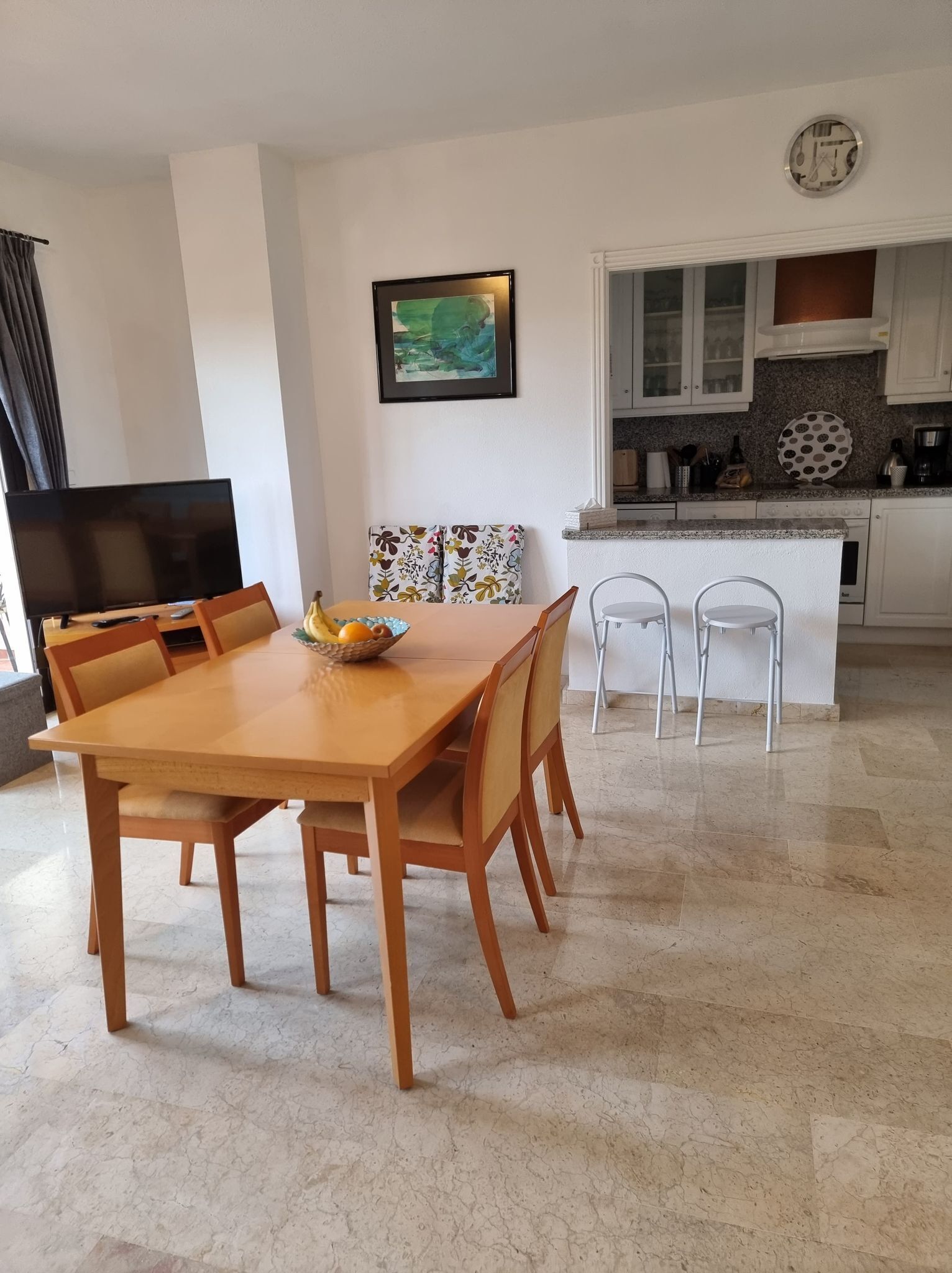 A dining area with a wooden table and chairs, a fruit bowl, and a television.