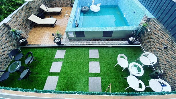 Une piscine sur le toit offrant une vue sur la ville, entourée de chaises longues et d’un petit espace aménagé en jardin.
