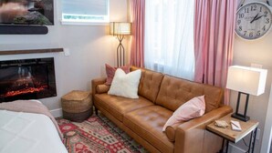 Ein gemütliches Hotelzimmer mit Ledersofa, Kamin, einer Uhr und Blick auf eine Berglandschaft.