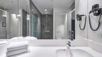 A modern bathroom with a large white sink, a glass shower enclosure, and a hairdryer mounted on the wall.