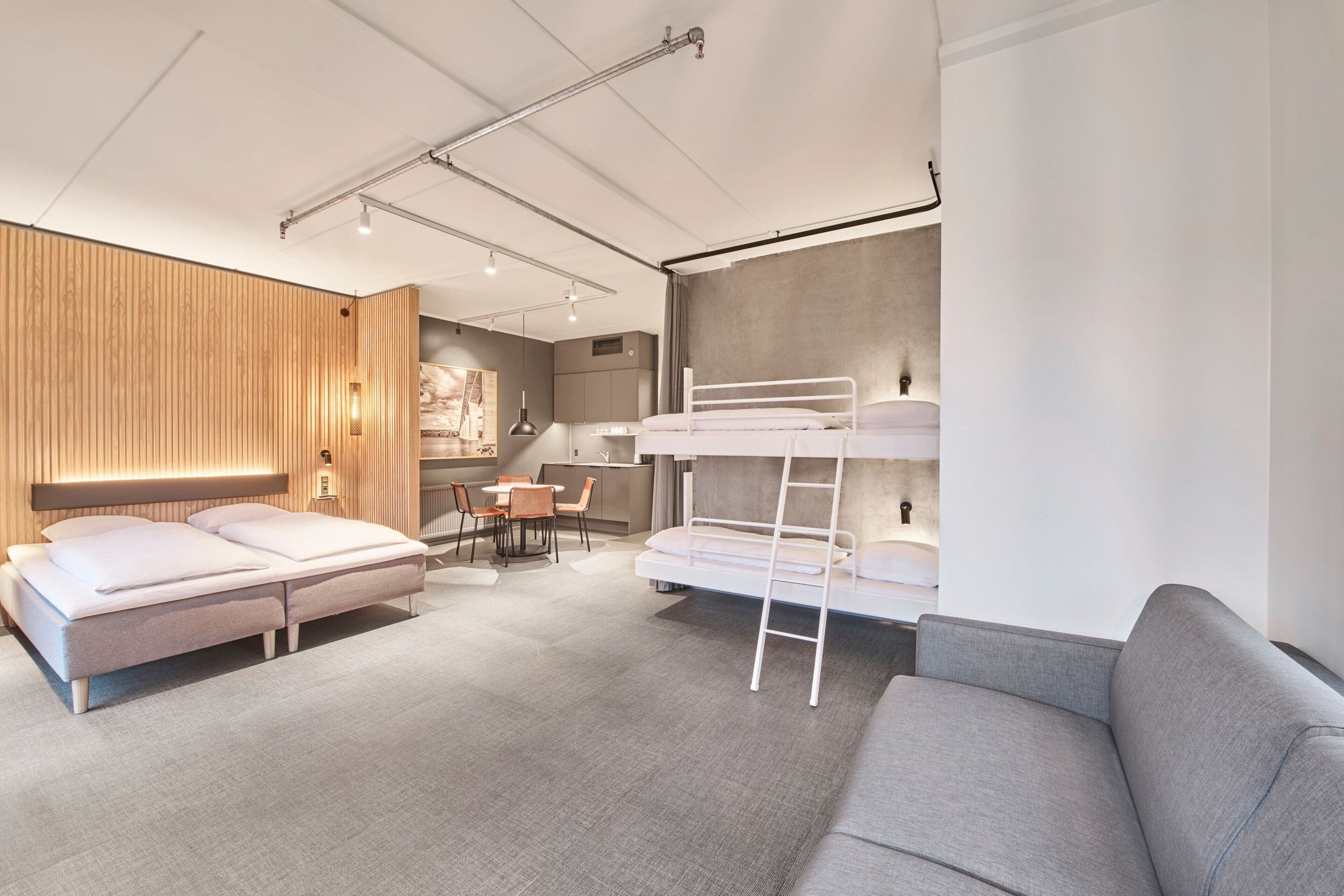 Ett modernt och kompakt hotellrum med en våningssäng, en soffa, ett skrivbord och en matplats.