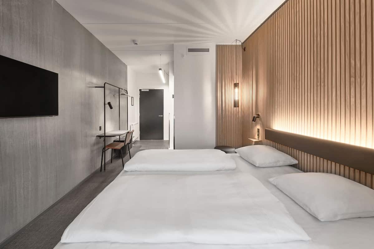 A modern hotel room with a large bed, a desk, and a mirror.