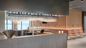 Un área de recepción moderna con un mostrador de madera, una lámpara de cristal y una zona de estar con sofá y mesas.