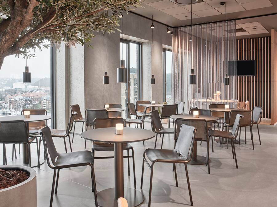 A modern dining area with round tables and chairs, a large tree, and a city view through large windows.