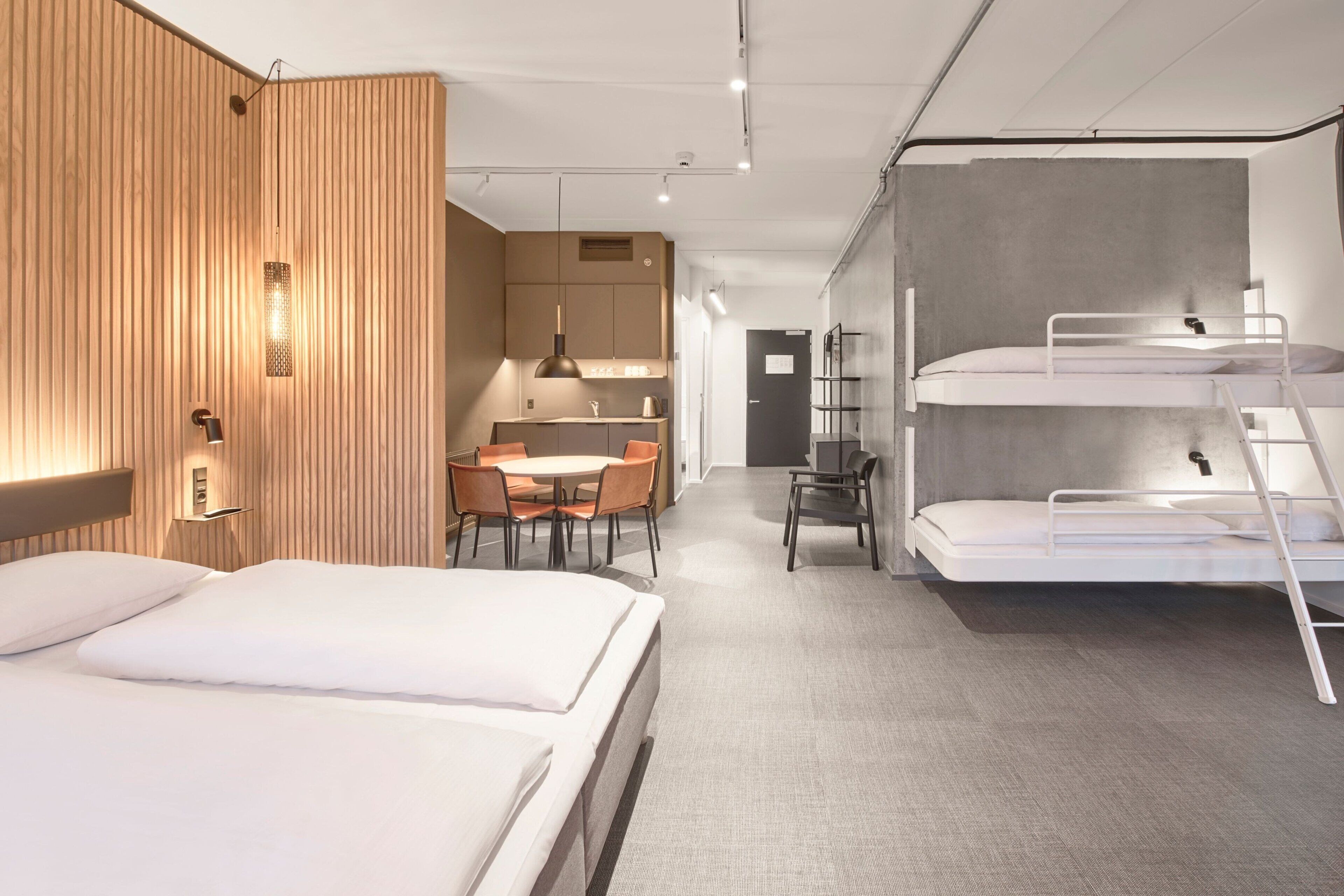 Ein modernes Hotelzimmer mit Stockbetten, einer Essecke und einer Küchenzeile.