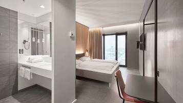 Una habitación de hotel moderna con una cama grande, un baño independiente con bañera, una mesa de comedor y vistas a la ciudad a través de la ventana.