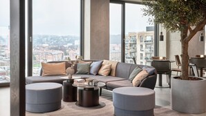 Una sala de estar moderna con un amplio sofá modular, otomanas redondas y una mesa de centro. Un ventanal ofrece vistas del paisaje urbano.
