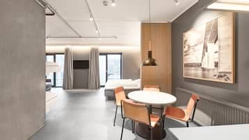 Una habitación de hotel moderna con una cama grande, una mesa redonda con sillas, una lámpara colgante y un cuadro grande en la pared.