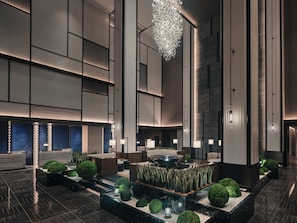 Un hall dâhĂŽtel moderne dotĂ© dâun espace salon central, dâun Ă©lĂ©ment dĂ©coratif aquatique et dâun grand lustre.