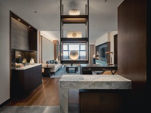 Una habitación de hotel moderna con una isla de cocina de mármol, un sofá, una mesa de comedor y un ventanal con vistas a la ciudad.