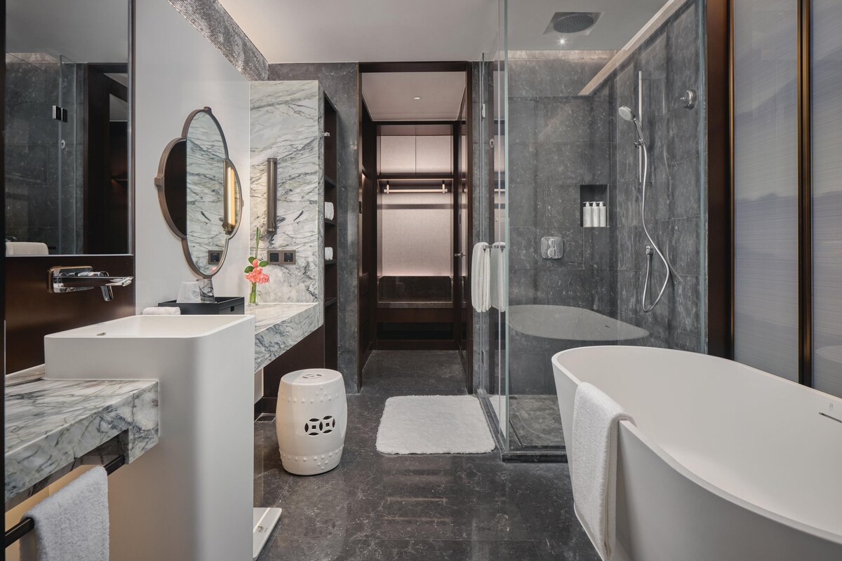 A modern bathroom with a marble vanity, a large mirror, a shower enclosure, and a bathtub.