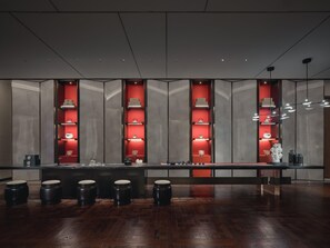 A modern interior with a long counter, red illuminated shelves, and black stools. - Hualuxe Kunshan Huaqiao (Suzhou)