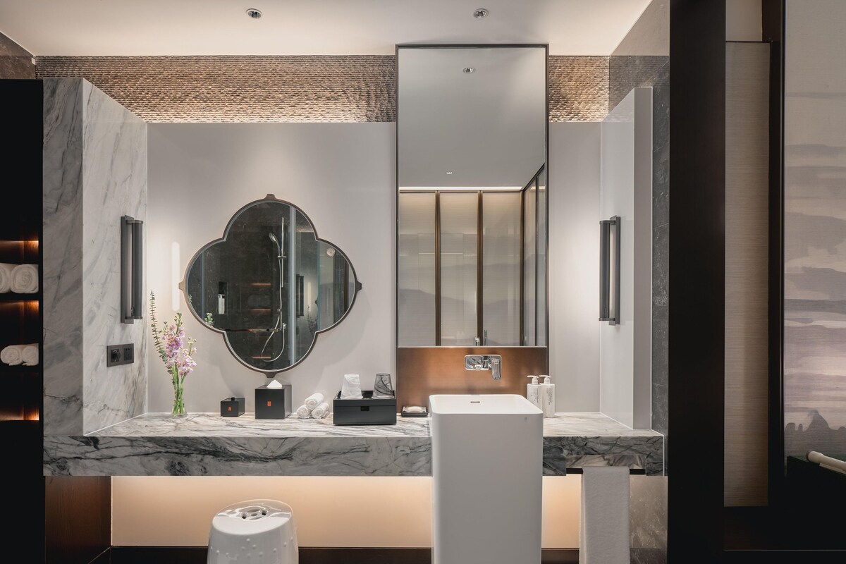 A modern bathroom with a marble vanity, a large mirror, a towel rack, and a scale.