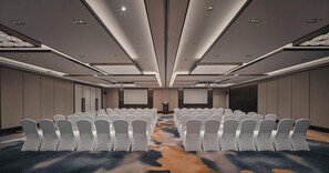 Un salón de conferencias con filas de sillas blancas, una pantalla grande y suelo alfombrado.