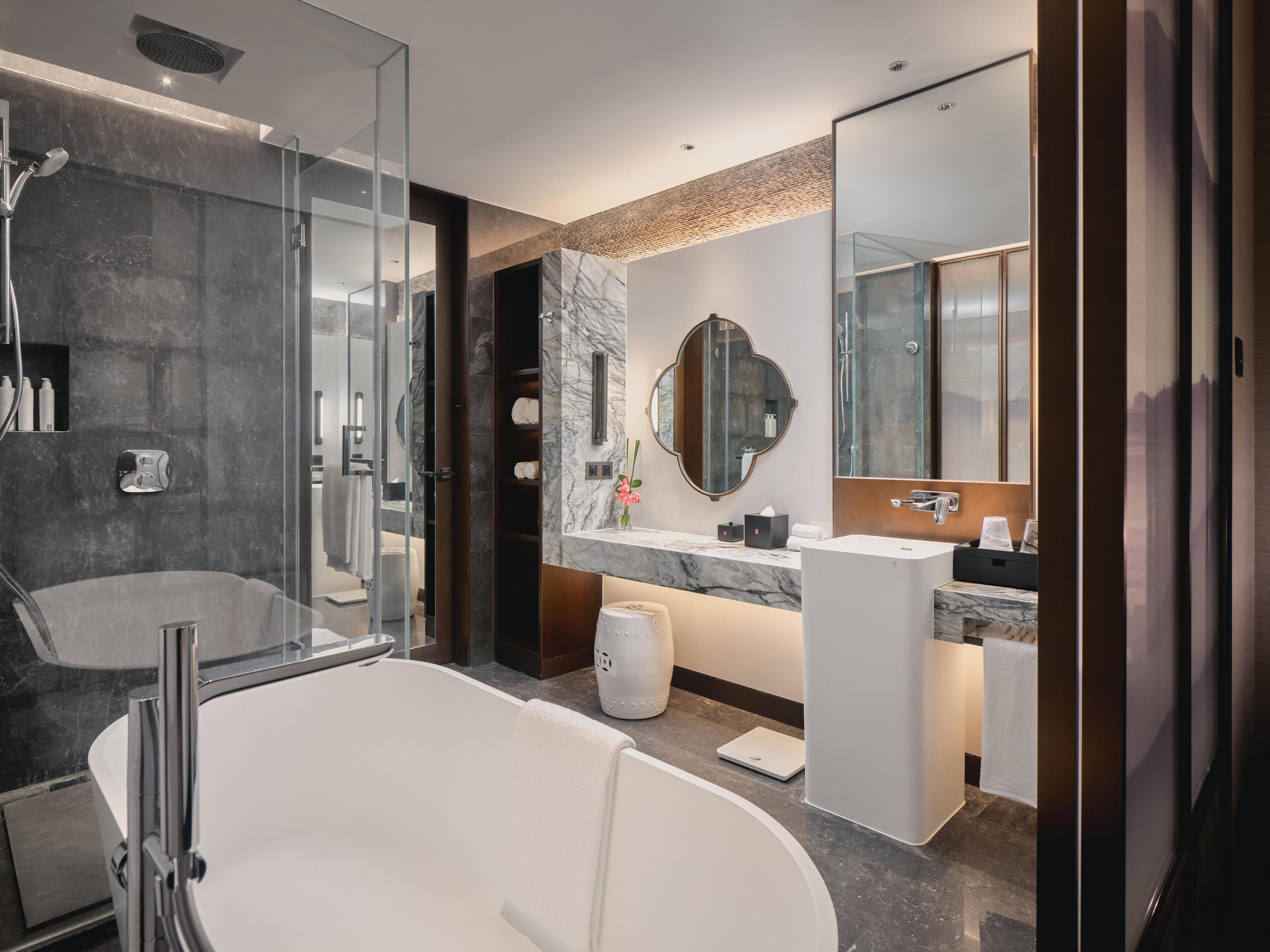 Un baño moderno con una bañera grande, zona de ducha independiente, tocador con espejo y encimera de mármol.