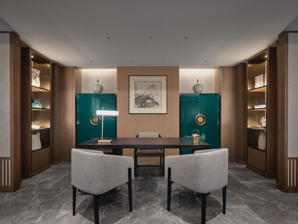 A conference room with a dark table, two chairs, a standing lamp, and teal cabinets with decorative items.