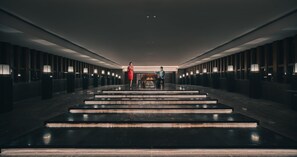 Un hall d’hôtel moderne avec un escalier central, des lambris en bois foncé et un éclairage encastré.