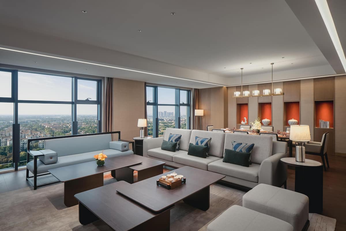 Une chambre d’hôtel moderne offrant une vue imprenable sur la ville, avec un ensemble de canapés, un coin repas et un espace bien éclairé.