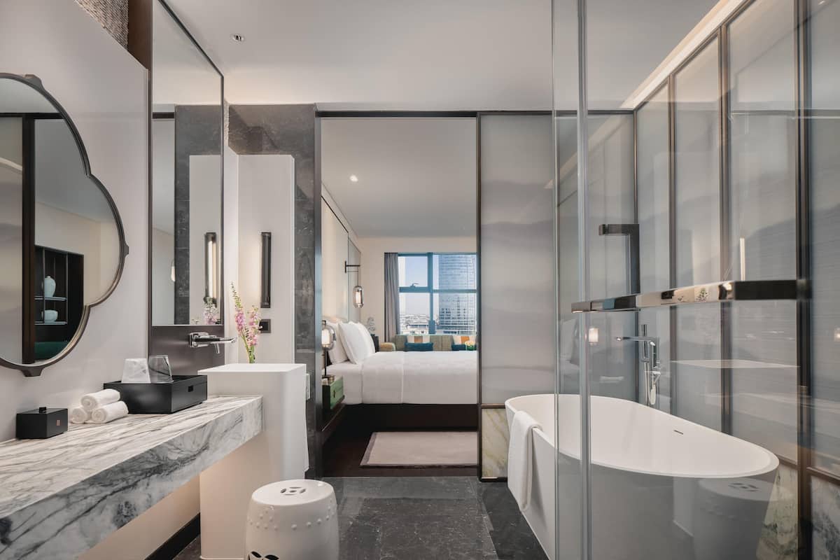 Une salle de bain moderne avec une grande baignoire, un comptoir en marbre, un miroir rond et une vue sur la ville.