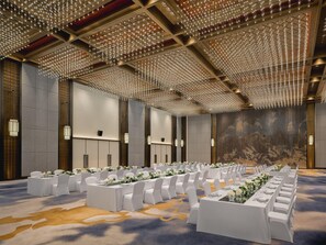 Un amplio salón de banquetes con filas de mesas dispuestas para eventos, una alfombra estampada y un techo con una estructura de luces.