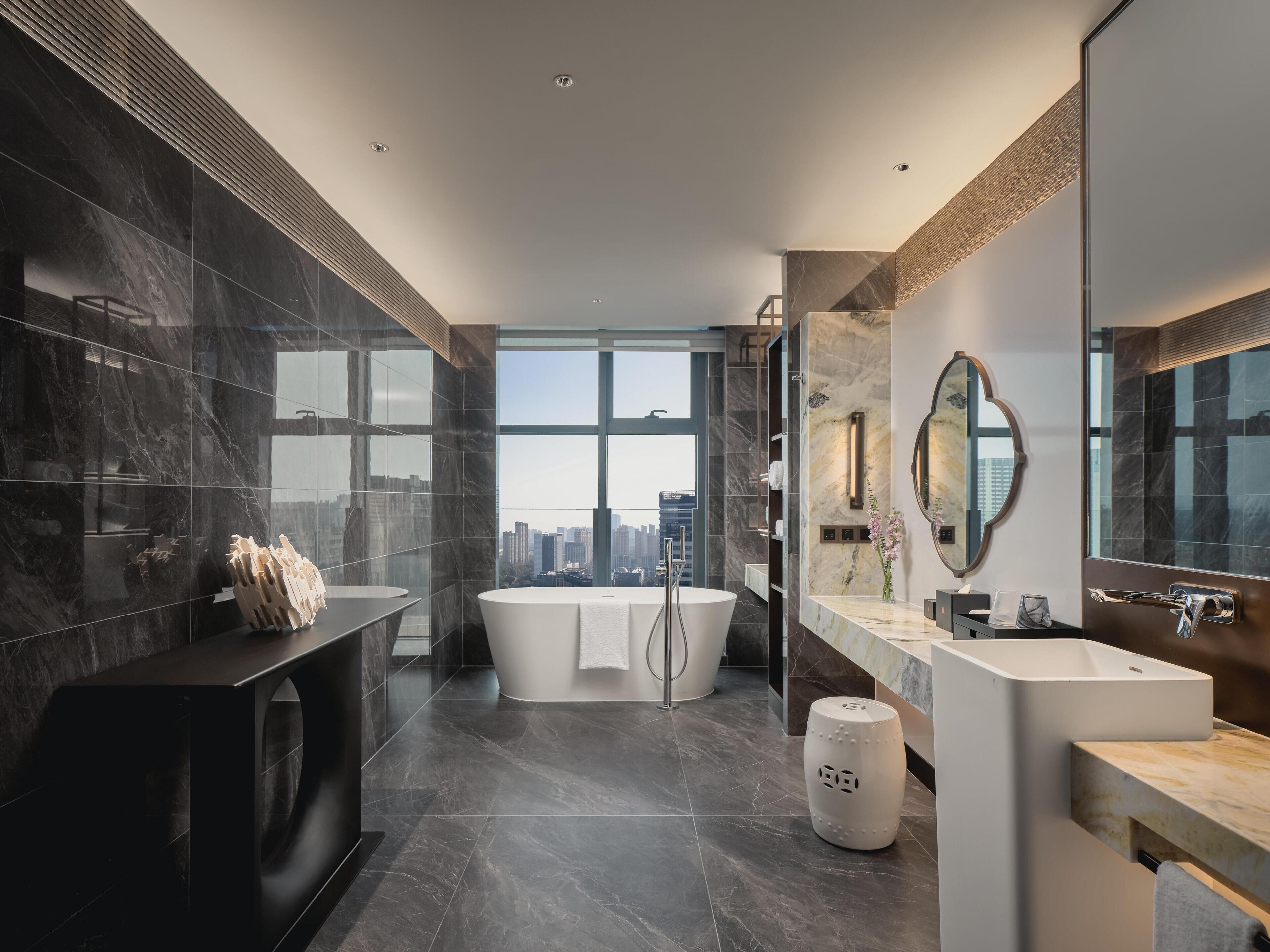 Un baño moderno con una bañera grande, un tocador con espejo y vistas a la ciudad.