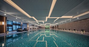 A large indoor swimming pool with a geometric tile pattern, modern ceiling design, and seating areas along the sides.