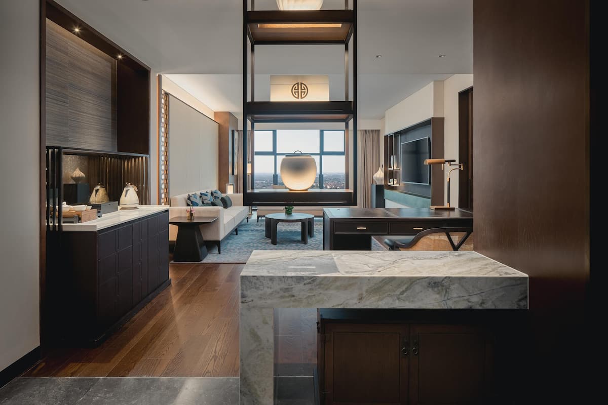 Une chambre d’hôtel moderne dotée d’un îlot de cuisine en marbre, d’un canapé, d’une table à manger et d’une grande fenêtre offrant une vue sur la ville.