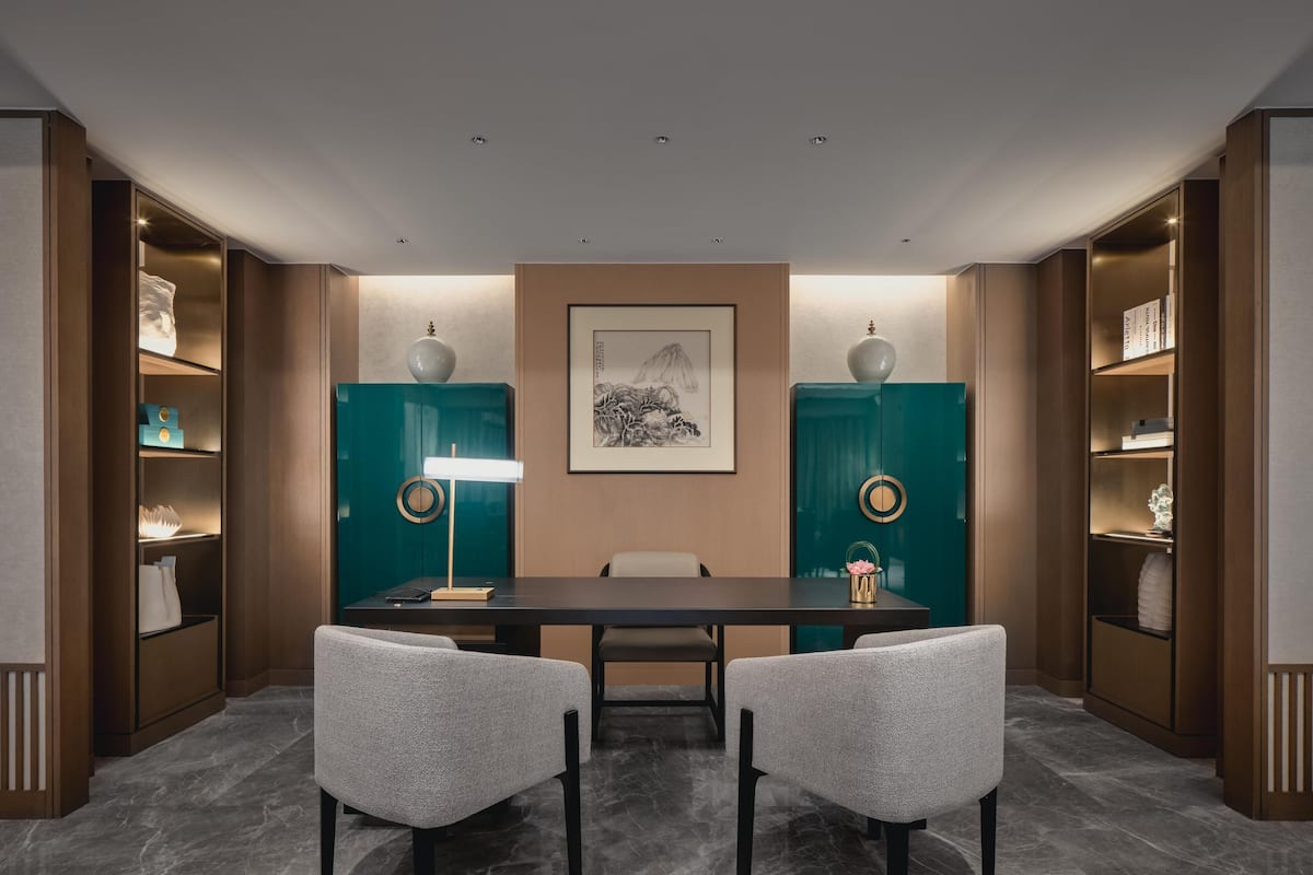 Une salle de conférence avec une table sombre, deux chaises, un lampadaire et des armoires de couleur turquoise ornées d’objets décoratifs.