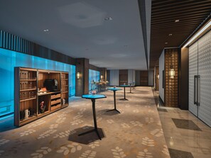 A modern hotel lobby with a long corridor, wooden cabinets, and tables with blue tops.
