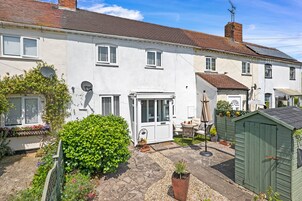 A white two-story house with a garden, a shed, and a patio area.