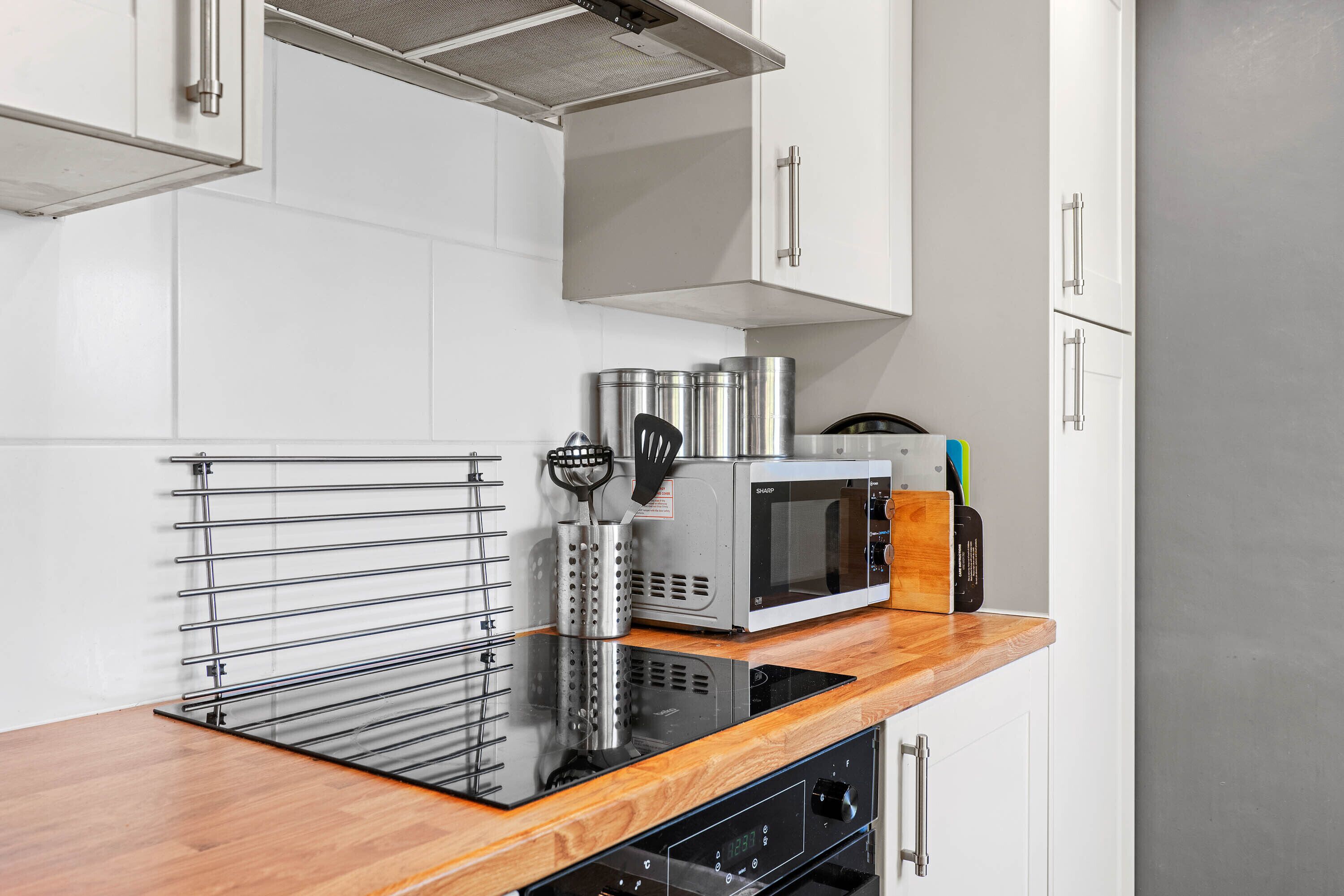 Una cocina con armarios blancos, una campana extractora de acero inoxidable, un microondas y una encimera de madera.