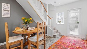 Ein Essbereich mit Holztisch, Stühlen und einer Blumenvase. Eine Treppe mit weißen Geländern führt zu einer Zwischenebene.