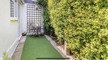 A small outdoor patio with a table and chairs, a potted plant, and a hedge.